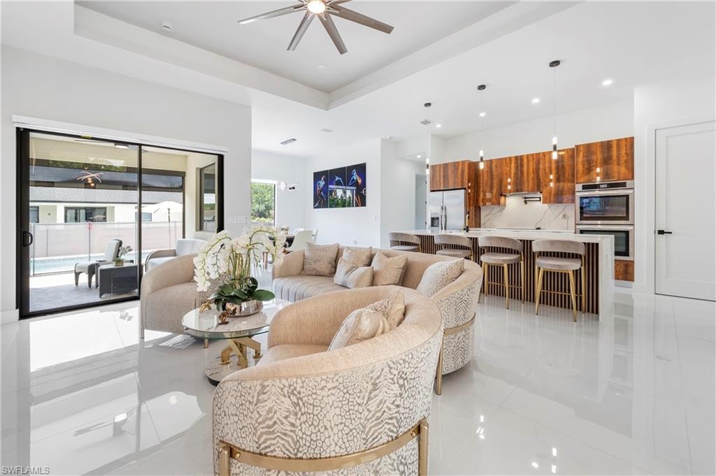 Open-concept living area featuring high-gloss tile flooring, a tray ceiling with a ceiling fan, and sliding glass doors opening to an outdoor patio with a pool