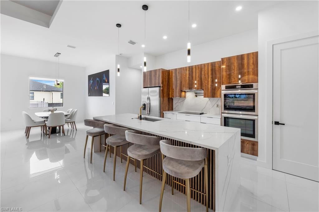 Modern kitchen featuring a waterfall island with a slatted wood-finish base, stainless steel appliances, wood-finish cabinetry, and white countertops with a subtle gray veining