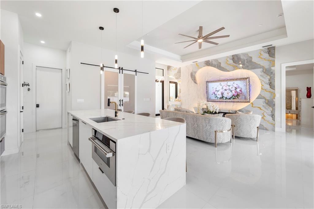 Open-concept living area featuring a large kitchen island with a built-in microwave, white tile flooring, and a decorative wall panel with integrated lighting