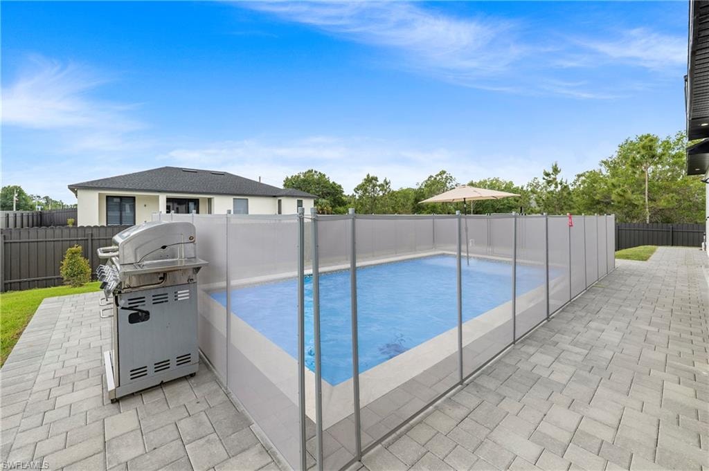 Outdoor swimming pool featuring a perimeter safety fence, paver patio, and a privacy fence