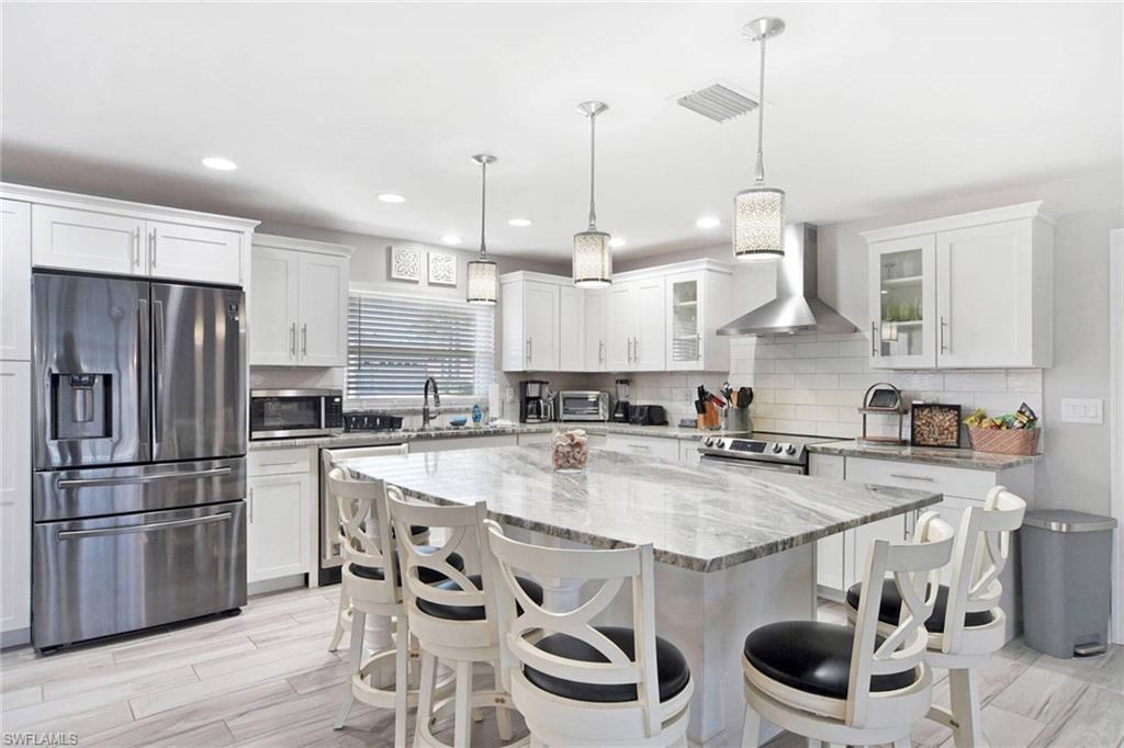 Kitchen with appliances with stainless steel finishes, light stone countertops, white cabinetry, wall chimney range hood, and recessed lighting