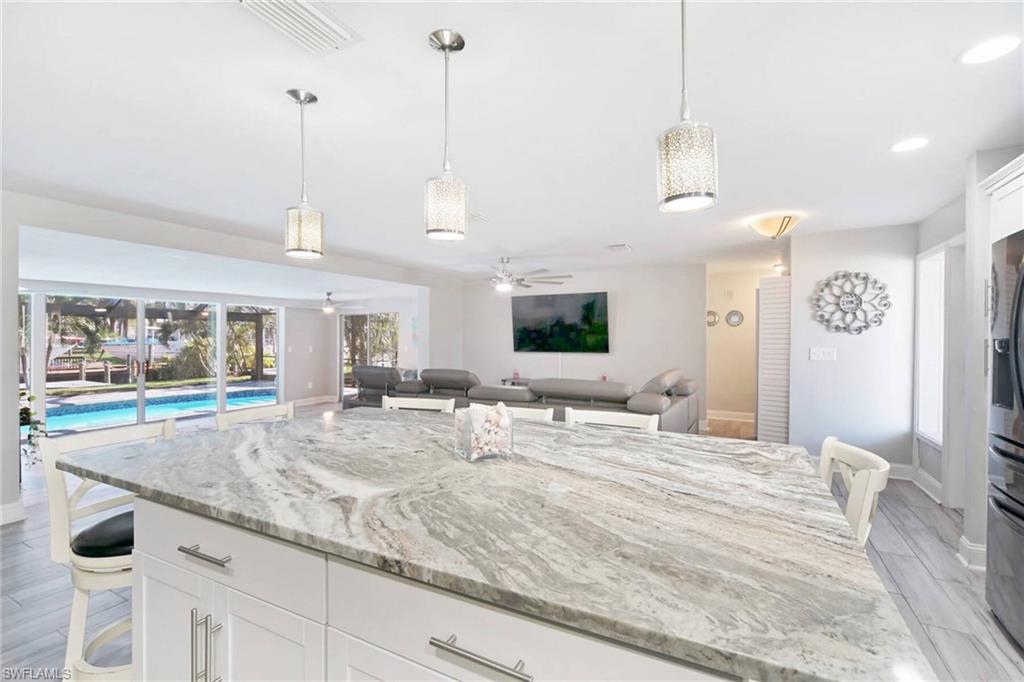 Kitchen featuring a breakfast bar area, white cabinets, light stone counters, pendant lighting, and wood finish floors