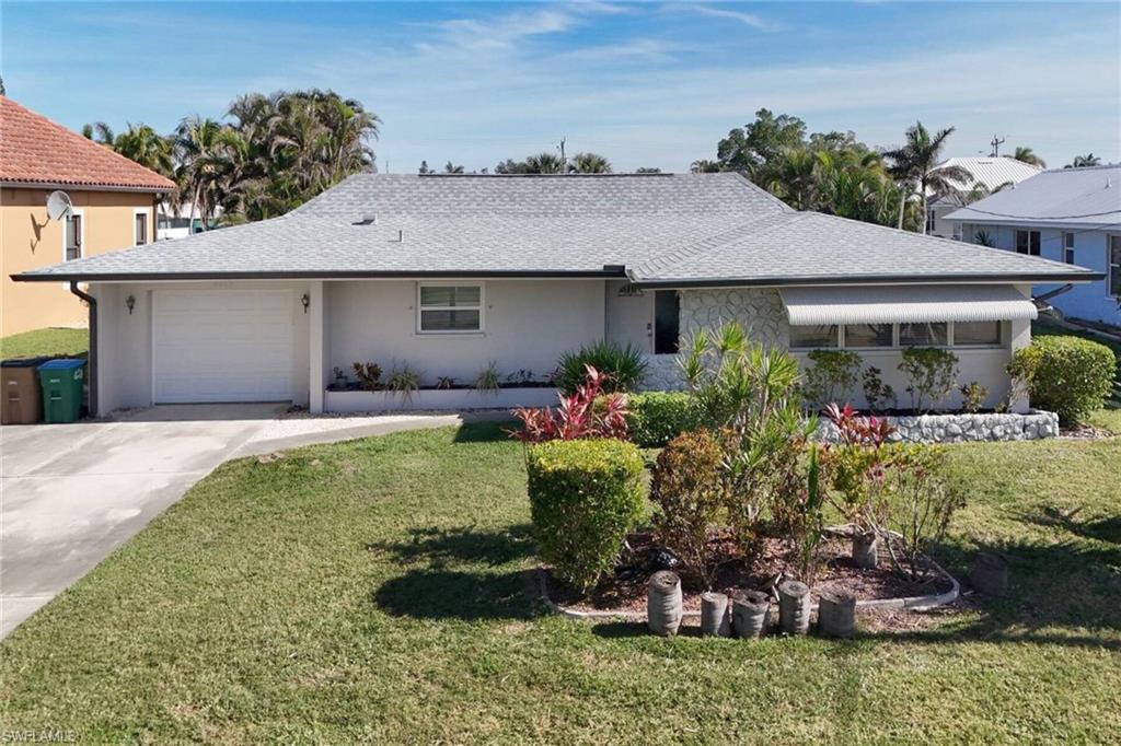 Ranch-style home featuring roof with shingles, an attached garage, and a front lawn