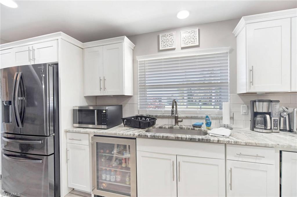 Kitchen featuring stainless steel appliances, beverage cooler, light stone countertops, white cabinetry, and backsplash