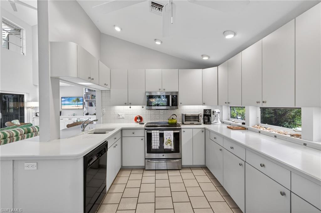 Kitchen featuring a peninsula, vaulted ceiling, stainless steel appliances, white cabinets, and decorative backsplash