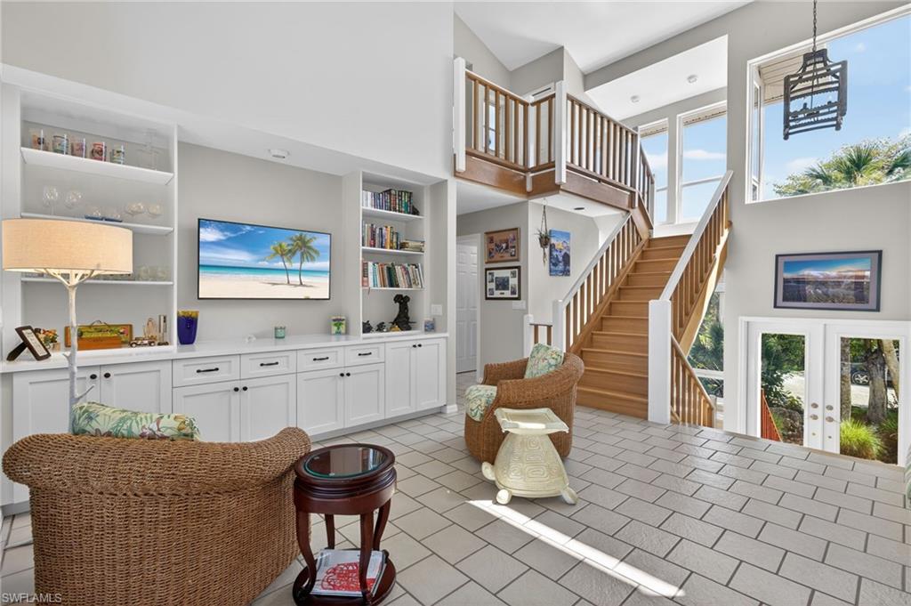 Living room with french doors, plenty of natural light, a high ceiling, light tile patterned floors, and built in shelves