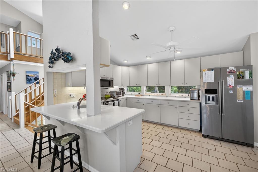 Kitchen featuring stainless steel appliances, light countertops, a kitchen breakfast bar, white cabinetry, and ceiling fan