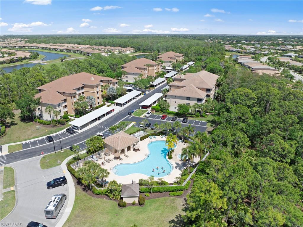 Aerial view of the property and its surroundings, featuring a community pool with an adjacent covered seating area, covered parking structures, and a lush green landscape with mature trees