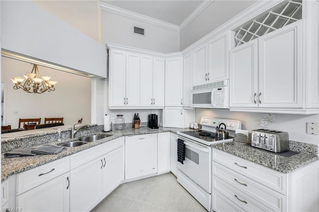 Kitchen with white cabinets, white appliances, ornamental molding, light stone counters, and light tile patterned floors