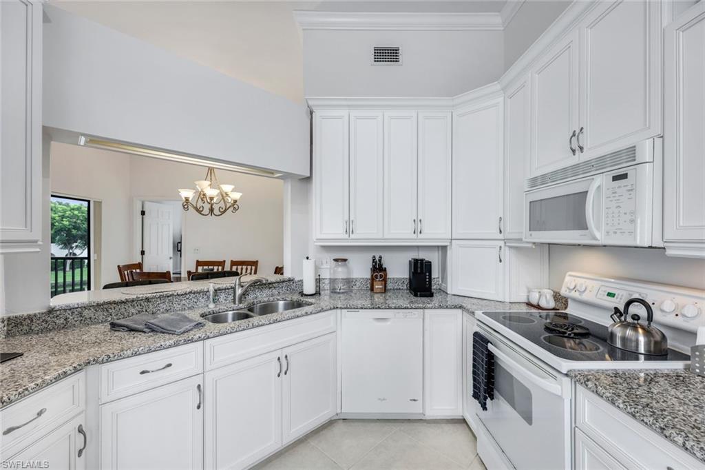 Kitchen with white cabinetry, white appliances, light stone countertops, sink, and ornamental molding