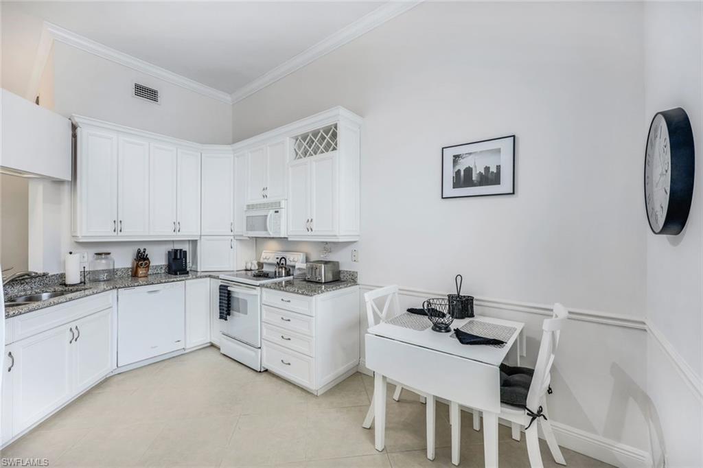 Kitchen with white appliances, sink, light stone countertops, white cabinetry, and ornamental molding