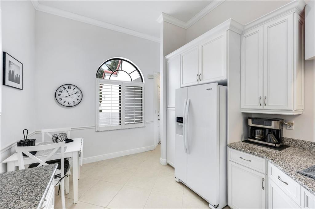 Kitchen featuring white cabinetry, ornamental molding, light tile patterned floors, and white fridge with ice dispenser