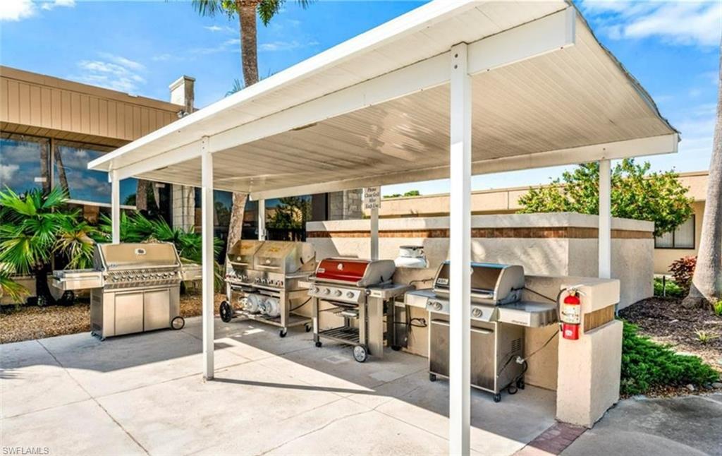 Outdoor grilling area featuring a white overhead canopy, several stainless steel grills, and a paved surface