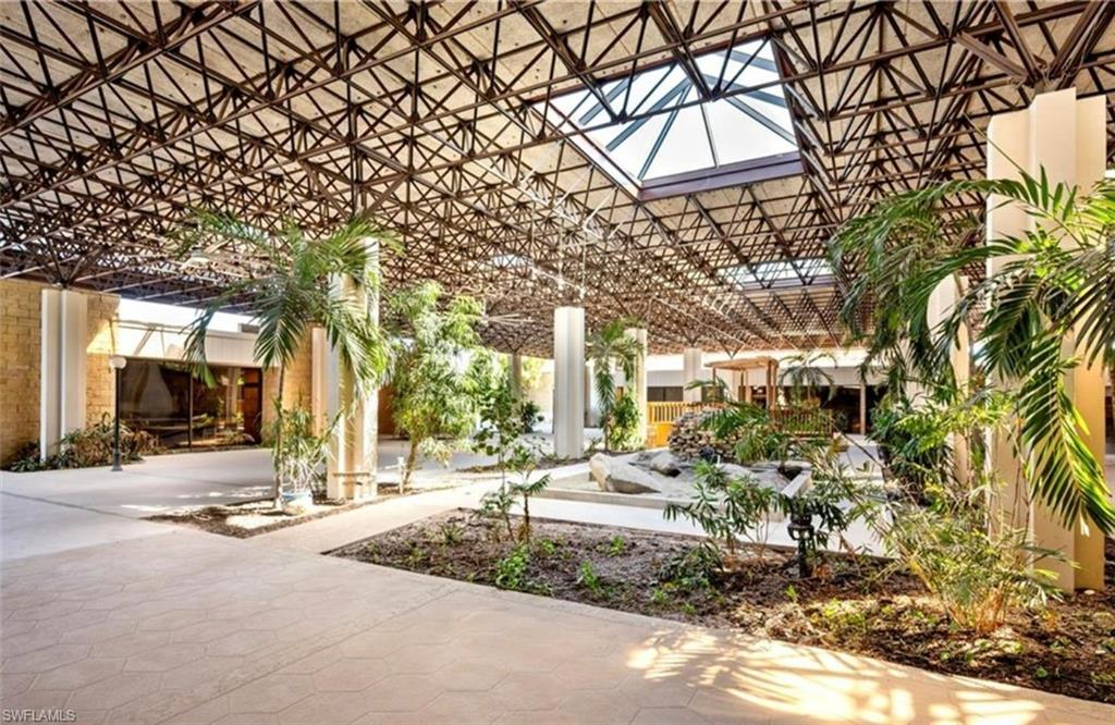 Spacious atrium featuring a geometric truss ceiling with skylights, extensive plantings, and a stone feature