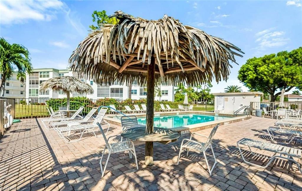 The property features a swimming pool surrounded by a paved patio with lounge chairs and a tiki umbrella