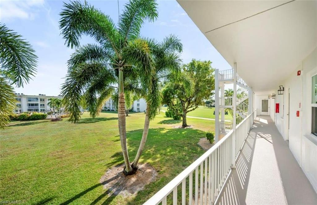 This property features a wide balcony with white railings, offering views of a well-maintained lawn with mature palm trees and additional landscaping