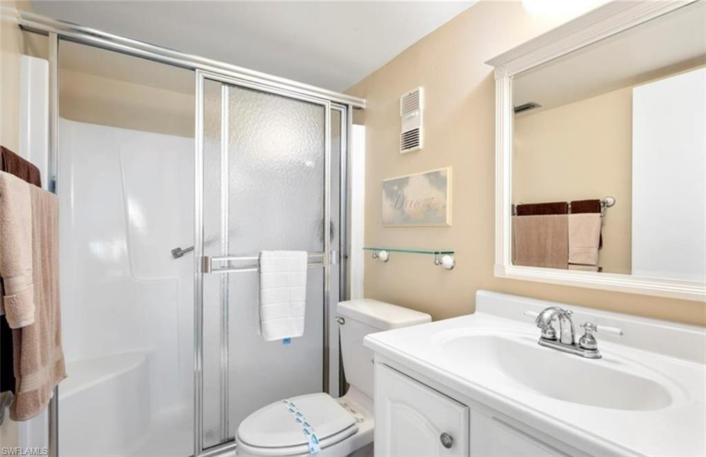 The bathroom features a shower with sliding glass doors, a vanity with a white countertop and integrated sink, and a framed mirror