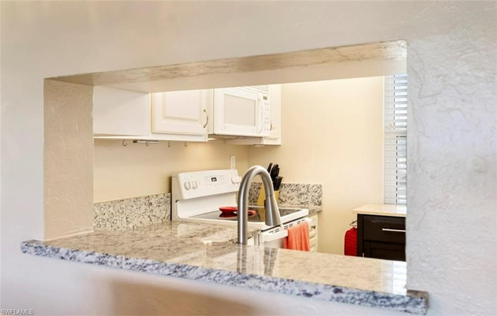 The kitchen features a pass-through window with a granite countertop, white cabinetry, and a white oven with an overhead microwave