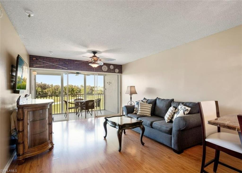 The living area features hardwood floors and provides access to a screened balcony through sliding glass doors, offering views of green landscaping