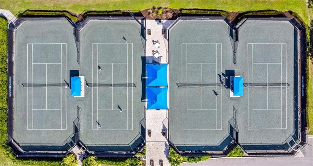 Aerial view of tennis courts, featuring four courts with blue shaded seating areas and surrounding greenery