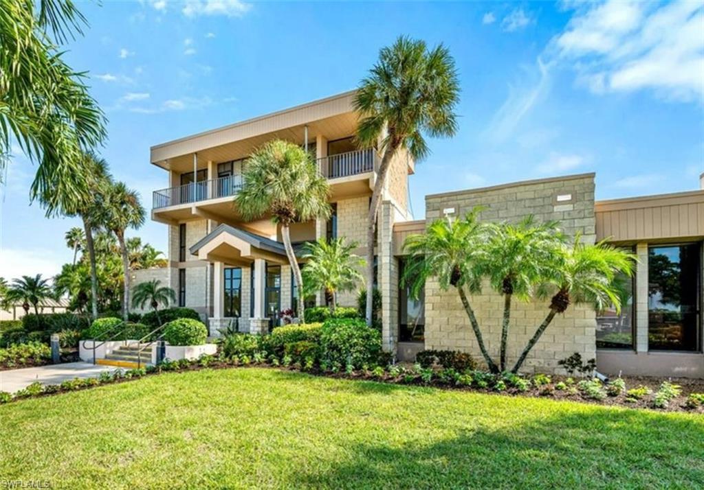 The property features a distinctive exterior with balconies and extensive landscaping, including a manicured lawn, lush shrubs, and various palm trees