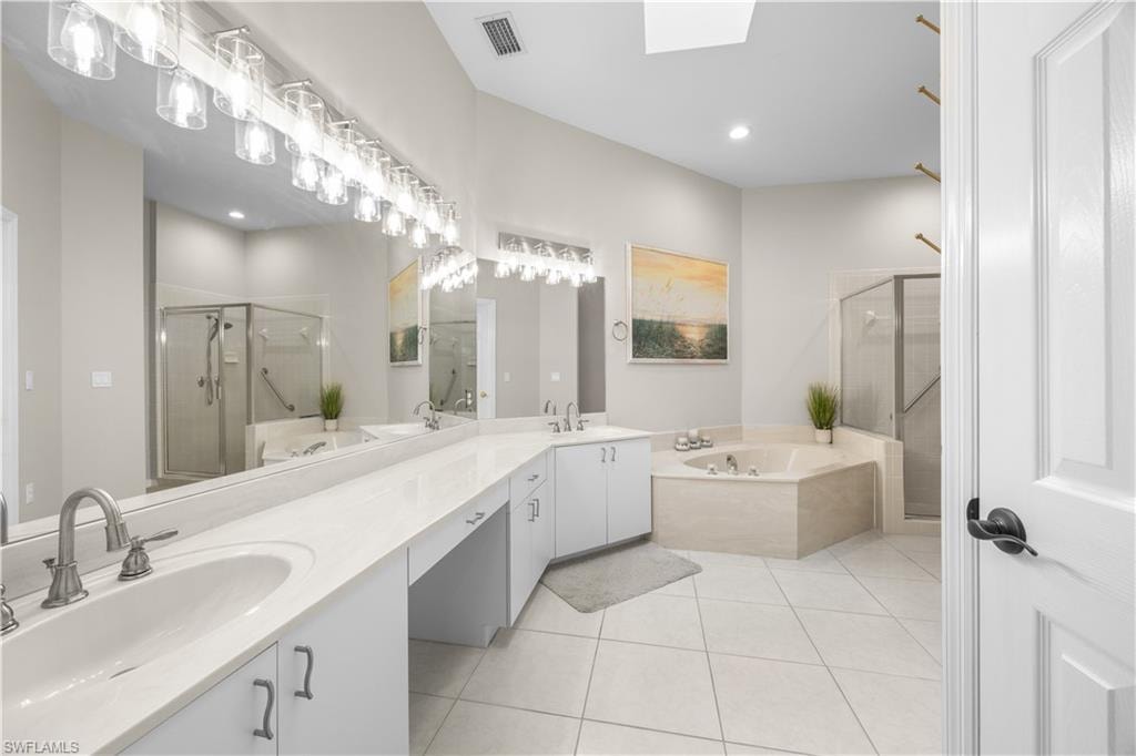 This bathroom features a spacious vanity with dual sinks, a large mirror with overhead lighting, a corner soaking tub, and a glass-enclosed shower