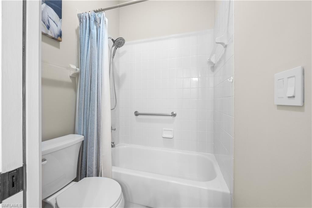 Bathroom featuring a bathtub with white tiled walls and a shower fixture, a white toilet, and a grab bar