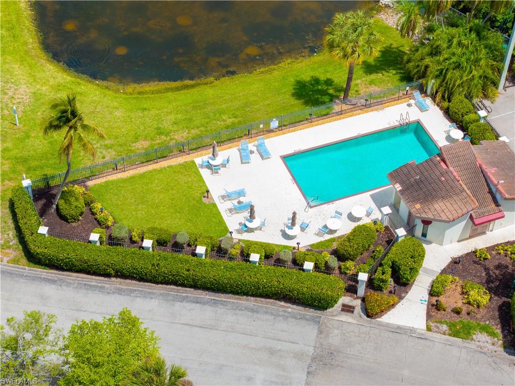 The property features a well-maintained outdoor community swimming pool and a poolside patio area with lounge chairs and tables, surrounded by lush green landscaping, including mature palm trees and manicured hedges