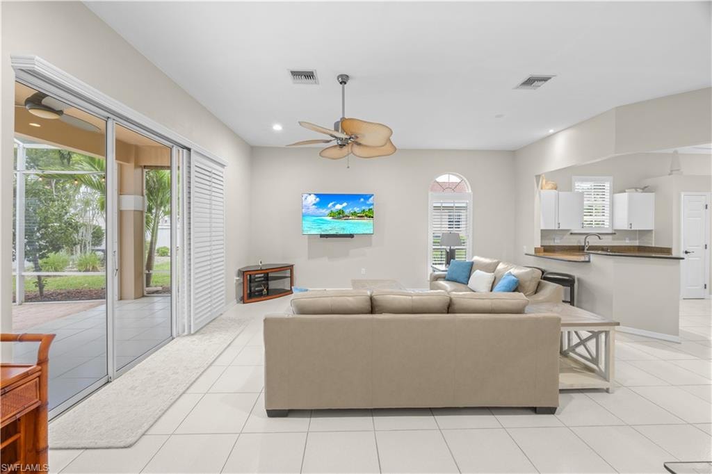 Living area featuring tiled flooring, a ceiling fan, and sliding glass doors leading to an outdoor patio with views of green landscaping