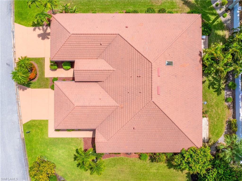 Aerial view of the property featuring a tiled roof, a large driveway, and a well-maintained lawn with mature trees