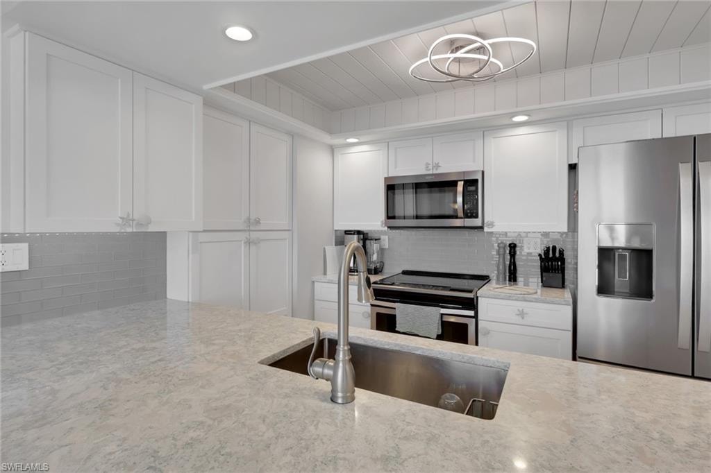 Contemporary kitchen featuring a large undermount sink with a gooseneck faucet, light-toned countertops, white shaker cabinetry, stainless steel appliances, and a subway tile backsplash