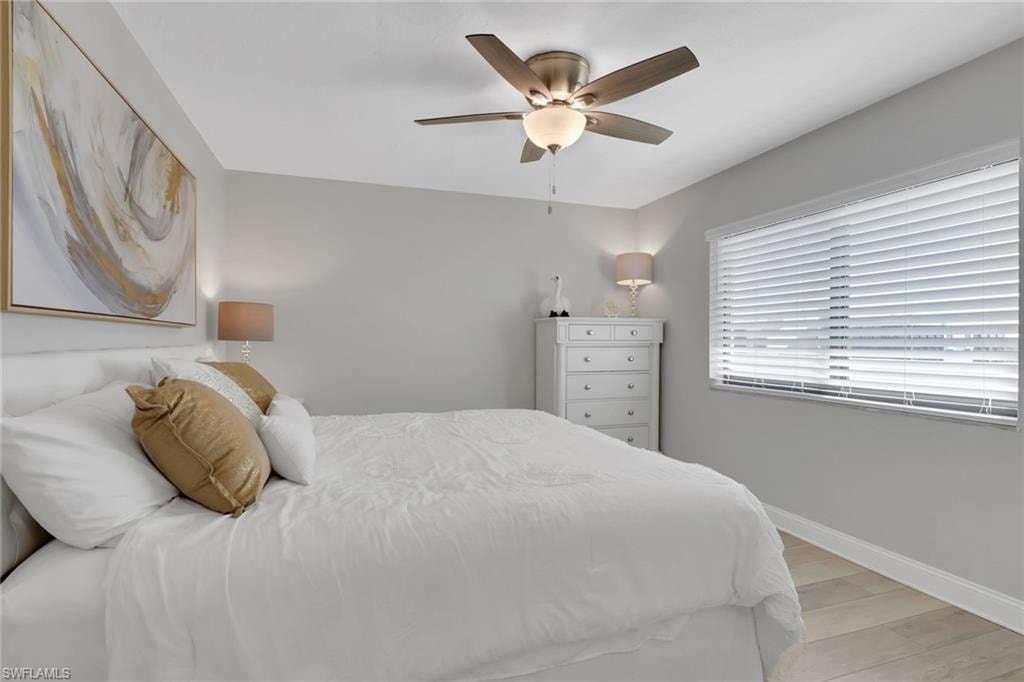 Bedroom featuring a ceiling fan with integrated lighting, wood-finish flooring, a window with horizontal blinds, and a neutral wall color