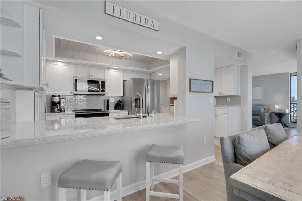 Kitchen featuring white cabinetry, stainless steel appliances, a grey tile backsplash, and light-toned countertops