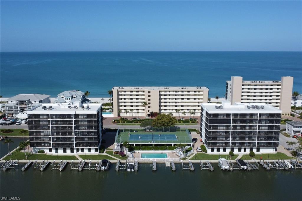 Waterfront condominium complex featuring multiple buildings with screened balconies, a marina with boat slips, a tennis court, and an outdoor swimming pool