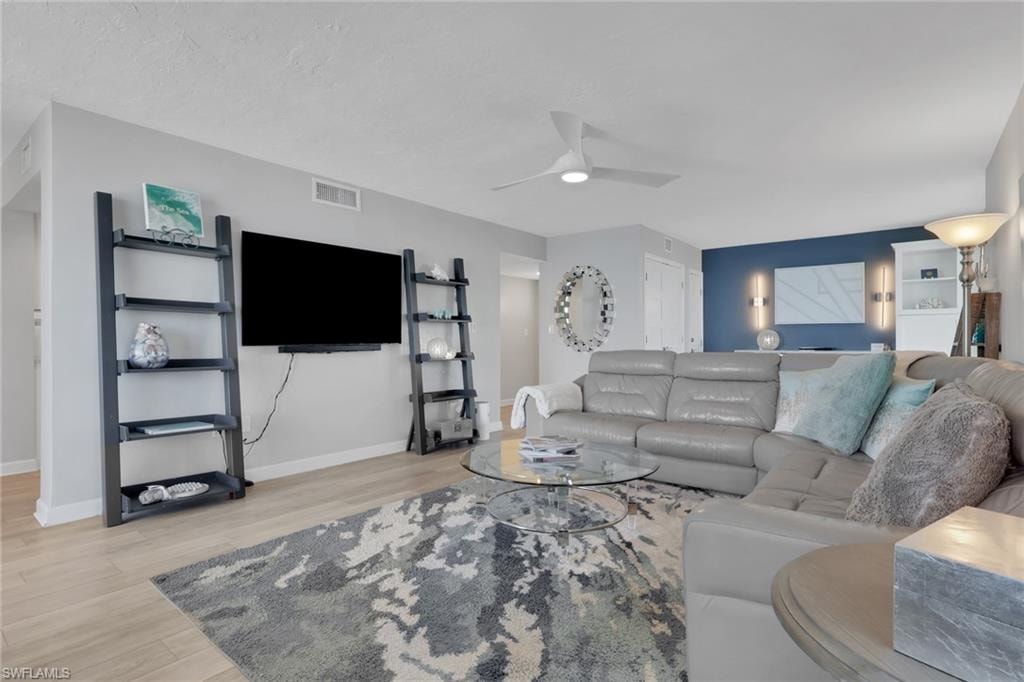 Open-concept living space featuring wood-finish flooring, a contemporary ceiling fan, and a built-in wall niche with sconce lighting