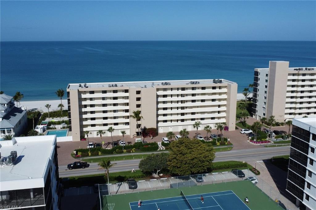 Beachfront condominium complex featuring a bright exterior, multiple balconies, a ground-level swimming pool, and landscaping with palm trees