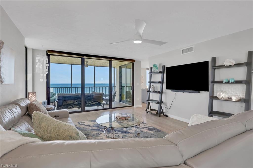 Spacious living area featuring floor-to-ceiling sliding glass doors, light wood-finish flooring, and a contemporary ceiling fan
