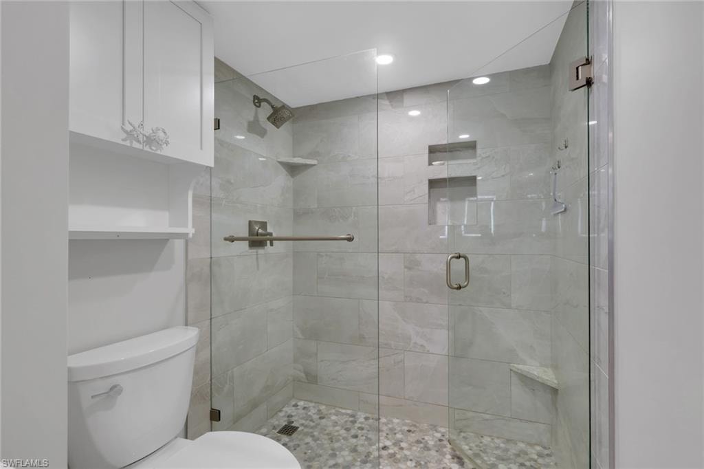 Glass-enclosed shower featuring a pebble-tiled floor, light-toned wall tiling, built-in recessed shelves, and a corner bench