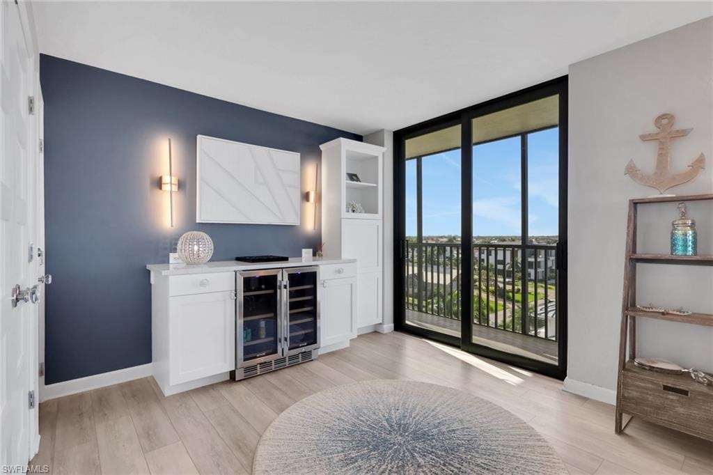 Built-in cabinetry with integrated beverage coolers, expansive sliding glass doors, balcony access, light wood-finish flooring, and contemporary wall sconces