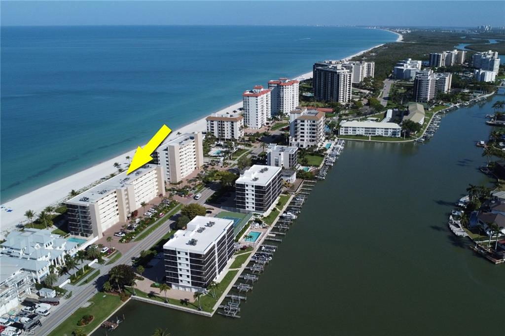 Waterfront condominium structure featuring direct beach access, a private parking area, and mature landscaping