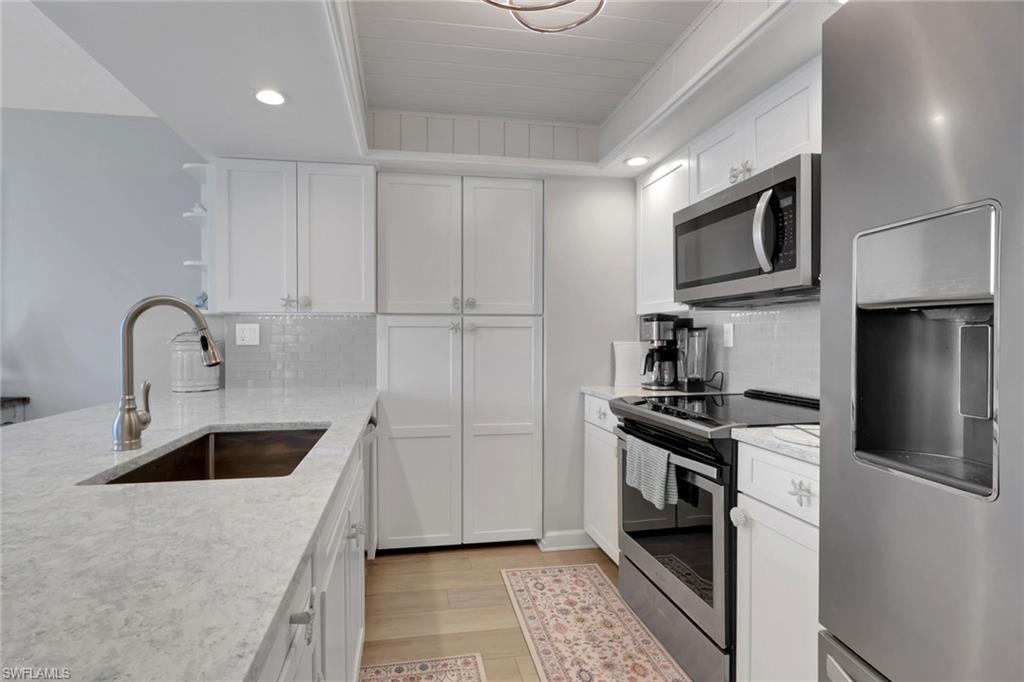 Bright kitchen featuring white cabinetry, light-toned countertops, stainless steel appliances, and a tile backsplash