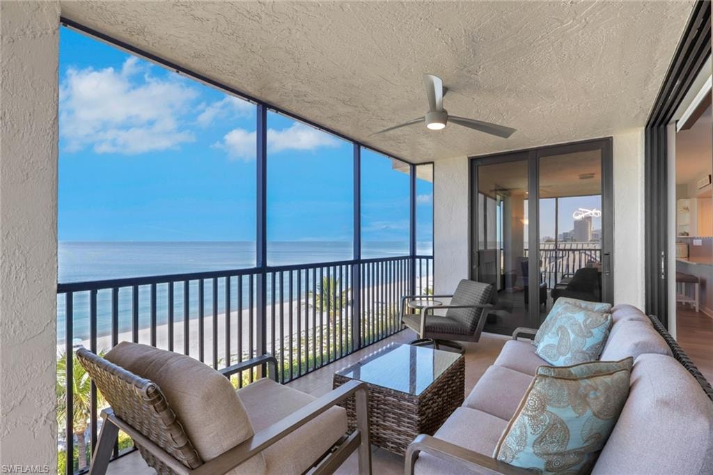 Screened balcony featuring a ceiling fan, white sand beach, and ocean backdrop