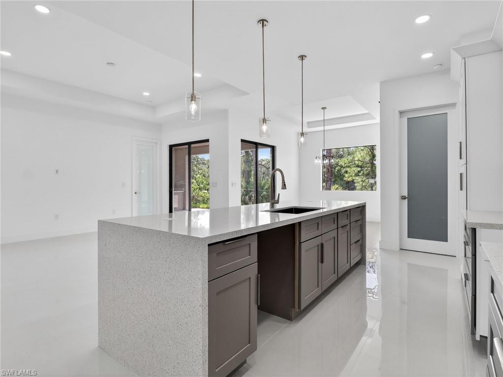 The kitchen features a large island with a light-colored countertop and dark cabinetry, pendant lighting, and a modern sink with a high-arc faucet
