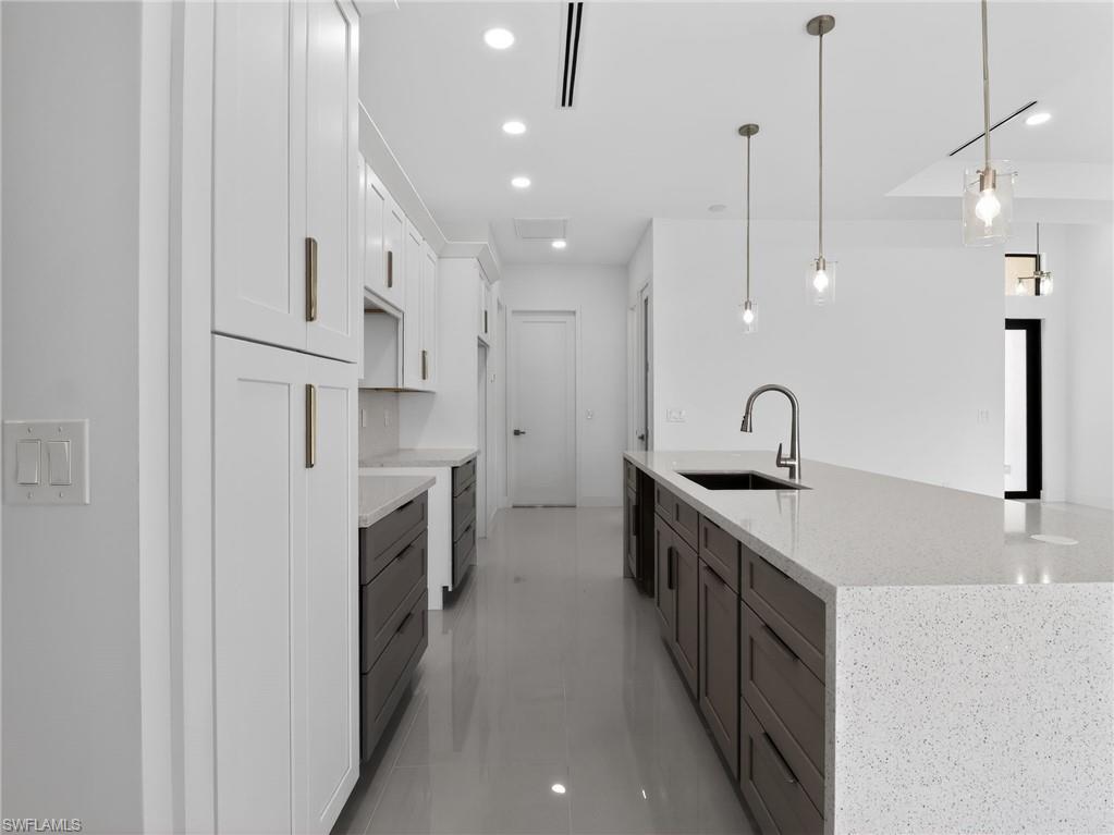 The kitchen features white shaker style upper cabinetry, dark lower cabinetry, light-colored countertops, a kitchen island with an integrated sink, and pendant lighting