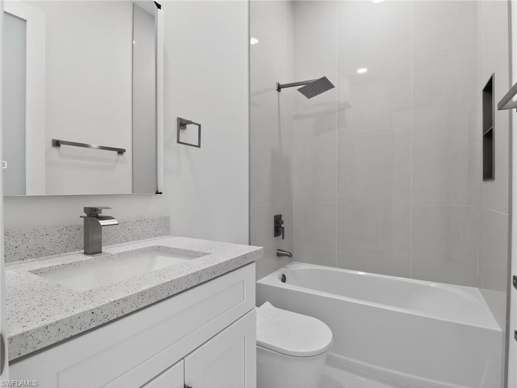 Bathroom featuring a vanity with a white countertop and an integrated sink, a rectangular mirror, a bathtub with a rainfall showerhead, and white tiled walls