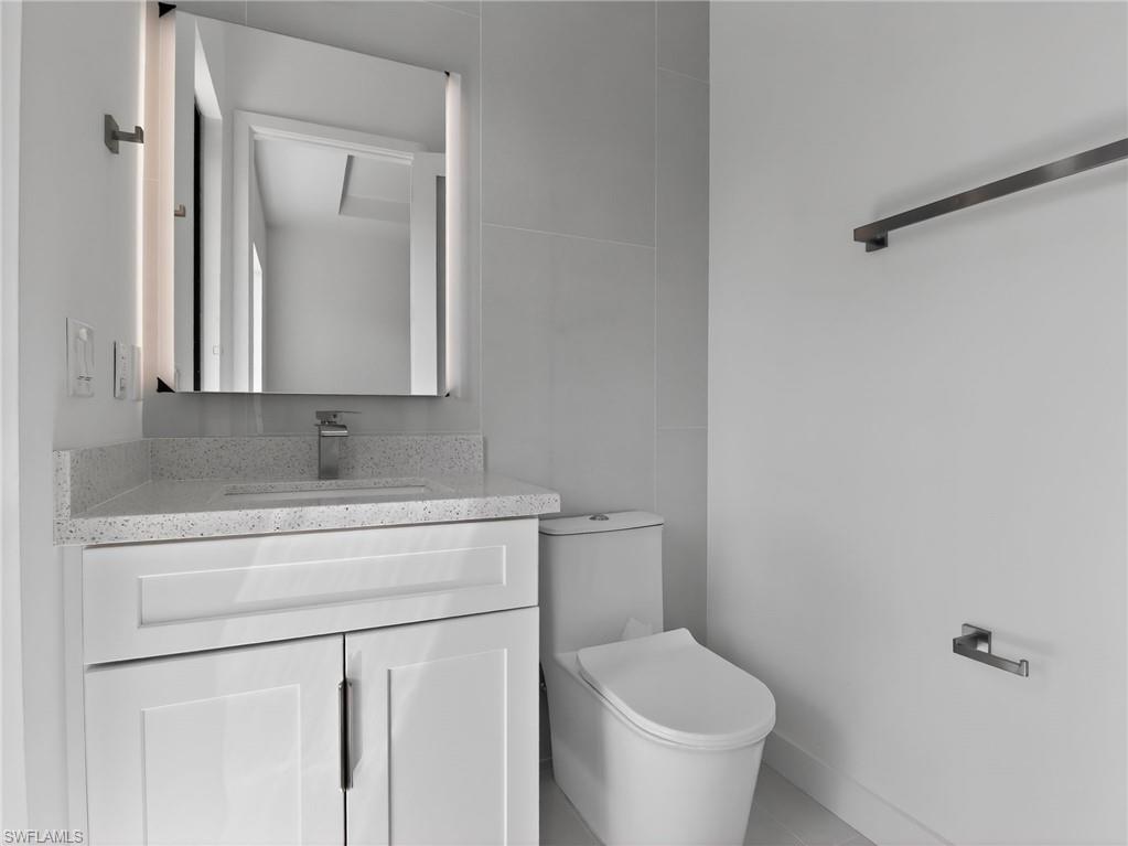 Modern bathroom vanity with a light speckled countertop, an integrated sink, and an illuminated mirror