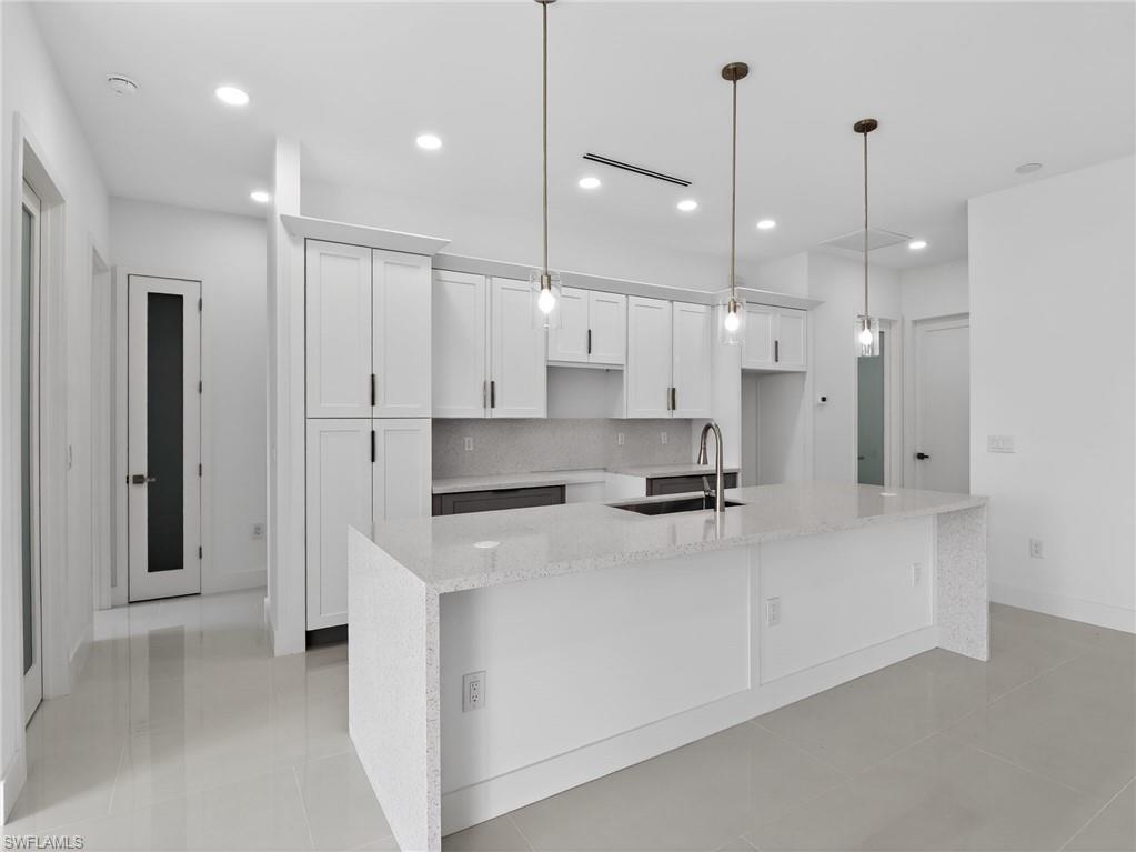 Modern kitchen featuring a large island with a sink and faucet, white cabinetry, and recessed lighting