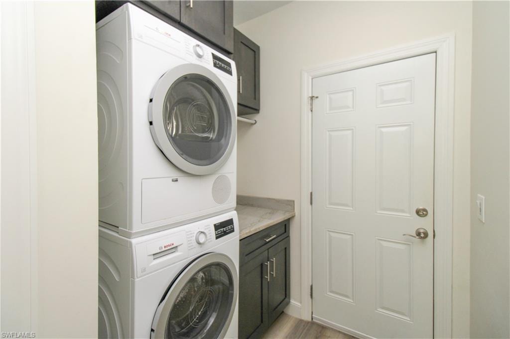 Clothes washing area featuring stacked washer and clothes dryer, light hardwood / wood-style floors, and cabinets