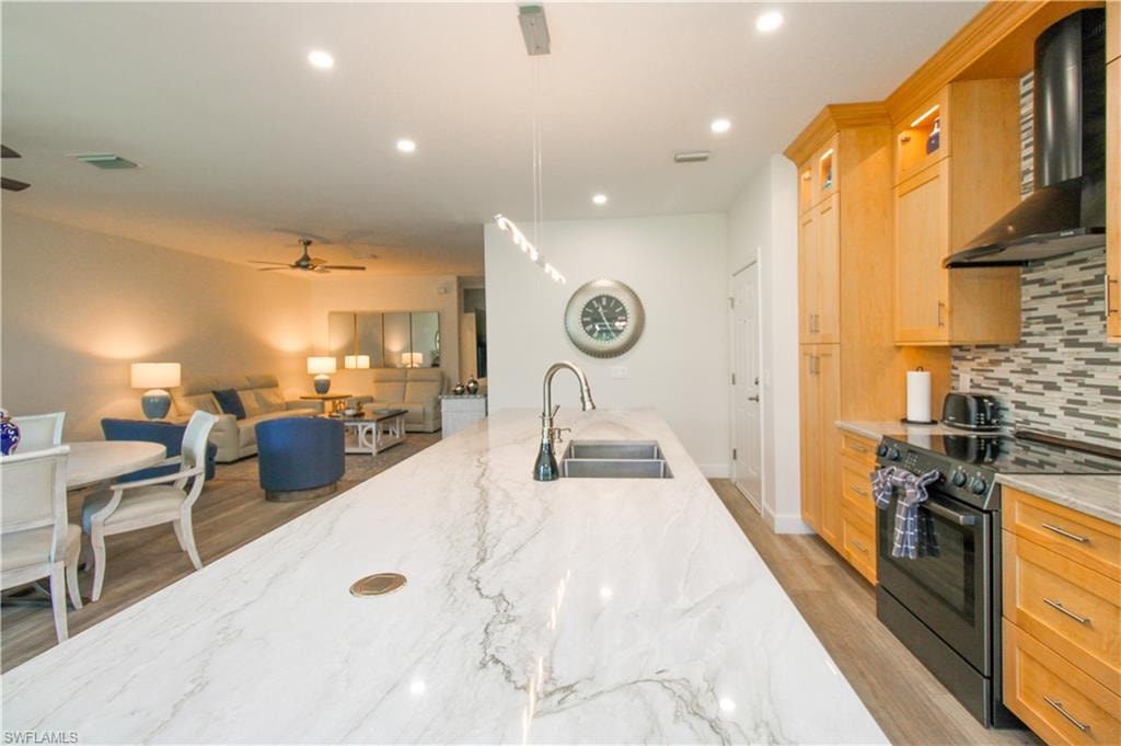 Kitchen featuring tasteful backsplash, black electric range oven, light stone counters, wall chimney range hood, and sink