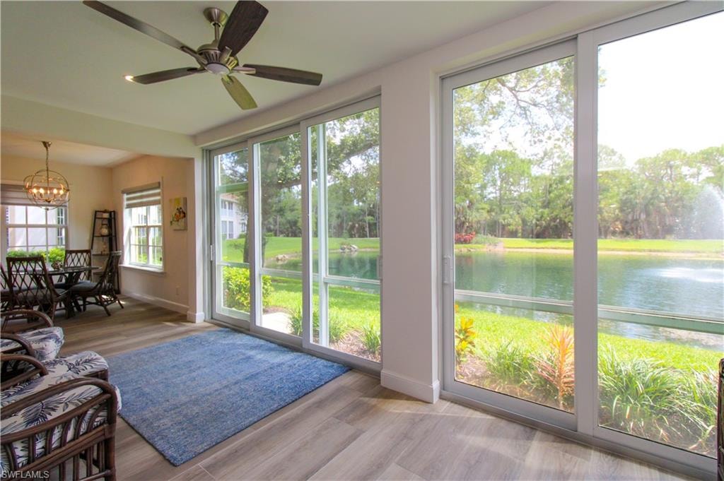 Sunroom / solarium featuring ceiling fan with notable chandelier and a water view